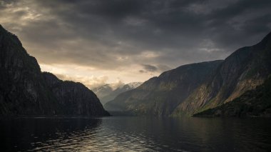 Sunset in the fjord and mountain landscape Eidfjord in Norway, sun rays falling through clouds