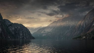 Man stand up paddling in the sunset in the fjord and mountain landscape Eidfjord in Norway, sun rays falling through clouds