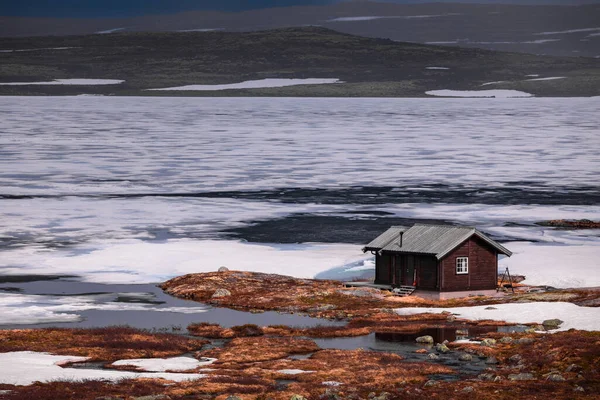 Hut at the waterfront of a frozen lake in the landscape of Hardangervidda National Park in Norway, snow and ice on the ground