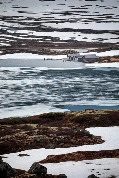Cabins at the waterfront of a frozen lake in the landscape of Hardangervidda National Park in Norway, snow and ice on the ground