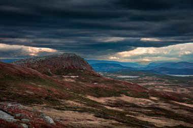 Mountain landscape of Jotunheimen National Park with red moss and dark cloudy sky during sunset in Norway