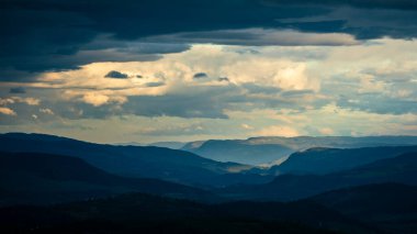 Mountain silhouette layers in the landscape of Jotunheimen National Park in Norway, dark and colorful clouds in the sky