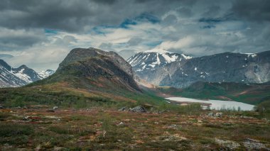 Mountain landscape with hike to Knutshoe summit in Jotunheimen National Park in Norway, snow covered mountains of Besseggen in background