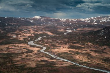 River Leirungsae with snow covered mountains in Jotunheimen National Park in Norway from above, dark clouds in sky