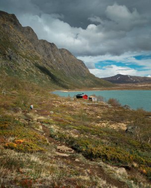 Woman hiking at turquoise lake surrounded by mountain landscape at Knutshoe summit in Jotunheimen National Park in Norway