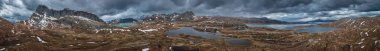 Panorama landscape with blue lakes, mountains and road of Jotunheimen National Park in Norway from above, dramatic dark cloudy sky