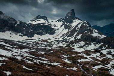 Mountain landscape of Litlefjellet Isfjorden with peak, road and snow in Norway Trollveggen, dramatic sky with dark clouds, from above