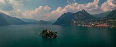 Isola di Loreto ile Iseo Gölü 'nde dağ manzarası. Dağlar ve Marone köyü. Gün boyunca mavi gökyüzü ve bulutlarla, İtalya. Haziran 2023