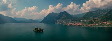 Isola di Loreto ile Iseo Gölü 'nde dağ manzarası. Dağlar ve Marone köyü. Gün boyunca mavi gökyüzü ve bulutlarla, İtalya. Haziran 2023
