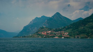 İtalyan İseo Gölü 'ndeki dağ manzarasında Eremo di San Pietro kilisesi ile Marone köyü, gökyüzünde bulutlarla öğleden sonra güneşi. Haziran 2023