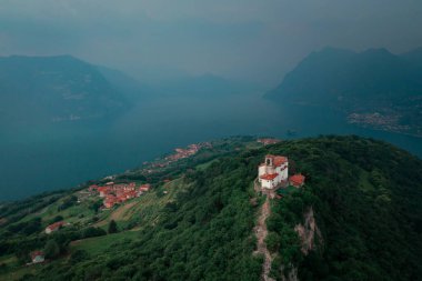 Chapel Santuario della Madonna della Ceriola yukarıdan Iseo Gölü 'nde Monte Isola Dağı' nın zirvesinde, arka planda dağlar ve göl, İtalya 'da baş döndürücü bulutlar. Haziran 2023