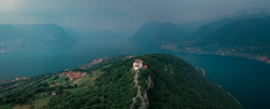 Chapel Santuario della Madonna della Ceriola yukarıdan Iseo Gölü 'nde Monte Isola Dağı' nın zirvesinde, arka planda dağlar ve göl, İtalya 'da baş döndürücü bulutlar. Haziran 2023