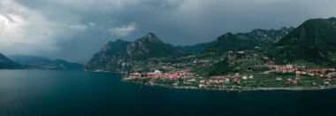 Iseo Gölü 'ndeki dağ manzarası. Dağlar ve Marone köyü. Gök gürültülü sağanak altında, kara bulutlar ve gökyüzü altında, İtalya. Haziran 2023