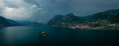 Isola di Loreto ile Iseo Gölü 'nde dağ manzarası. Dağlar ve Marone köyü, kara gökyüzü ve bulutlar altında fırtına sırasında, İtalya. Haziran 2023