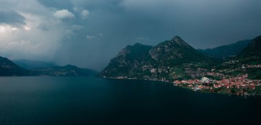 Iseo Gölü 'ndeki dağ manzarası. Dağlar ve köy Marone, gök gürültülü sağanak yağış sırasında kara gökyüzü ve bulutlar, İtalya