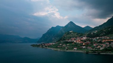 Iseo Gölü 'ndeki dağ manzarası. Dağlar ve Marone köyü. Yukarıdan, kara gökyüzü ve bulutlarla, İtalya. Haziran 2023