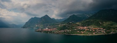 Iseo Gölü 'ndeki dağ manzarası. Dağlar ve Marone köyü. Yukarıdan, kara gökyüzü ve bulutlarla, İtalya. Haziran 2023
