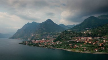 Iseo Gölü 'ndeki dağ manzarası. Dağlar ve Marone köyü. Yukarıdan, kara gökyüzü ve bulutlarla, İtalya. Haziran 2023