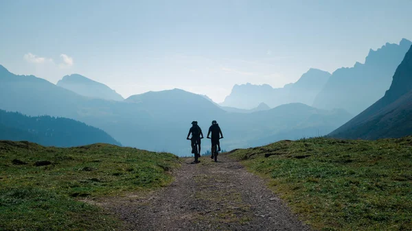夏季阳光明媚的蓝天 奥地利蒂罗尔 卡文德尔山区蓝天前两名骑山地自行车的男子的相貌 图库照片