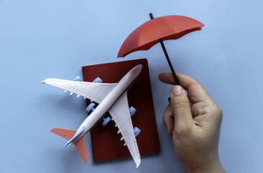 Seyahat sigortası konsepti. İyi yolculuklar. Uçuş gecikmeleri, iptal, bavul hasarı, kayıp, kaza ve sağlık harcamaları. Uçak ve pasaportun kırmızı şemsiye örtüsü