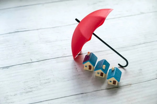 Concept of renters home insurance or mortgage protection. House under a red umbrella.