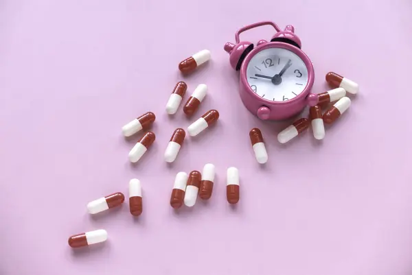 Reminder to take medicine on time, pharmacy, supplements or vitamins. Alarm clock with pills on pink background.
