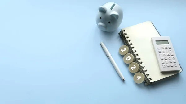 Saving goal for new year. Financial Planning for 2024. Piggybank , notebook and calculator on a blue background with copy space.