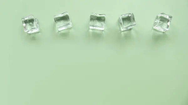 Concept of cold and refreshing. Ice cubes with water drops on a green background.