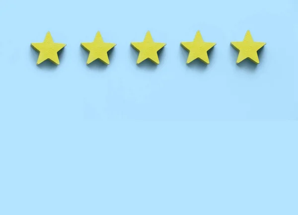 Client feedback, product rating, customer experience satisfaction. Five yellow wooden star on blue background with copy space.
