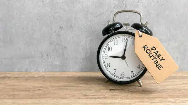 Çalar saat kravatı, üzerinde 'Günlük rutin' yazan kopya alanı olan ahşap masa.