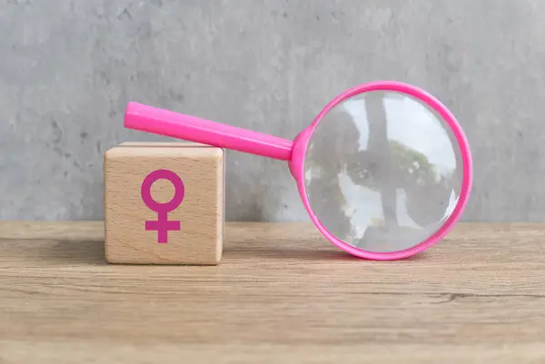 Menopoz kavramı ahşap bir küpün üzerinde pembe büyüteç ve tahta bir masa üzerinde kadın sembolü..