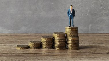 Yükselen altın sikkelerin tepesinde duran minyatür işadamı ya da profesyonel.