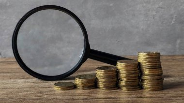 Yükselen altın sikkeler ve ahşap masanın üzerinde büyüteç.