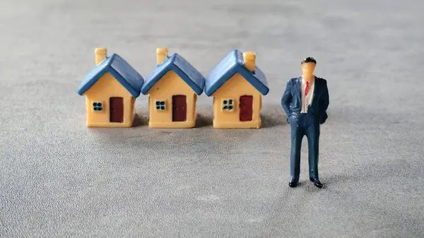 Minyatür bir evin önünde duran bir iş adamı..