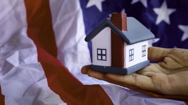 Amerikan bayrağının arka planında el ele tutuşan bir model ev..