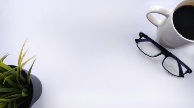Minimalist düz çalışma alanı, bitki, gözlük ve beyaz üzerine bir fincan kahve içerir. İş, planlama, üretkenlik, zaman yönetimi, geniş kopya alanı ile günlük gündem için ideal.