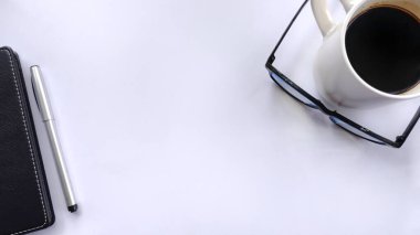 Kalem, defter, gözlük ve beyaz üzerine bir fincan kahvenin yer aldığı minimalist düz çalışma alanı. İş, planlama, üretkenlik, zaman yönetimi, geniş kopya alanı ile günlük gündem için ideal.