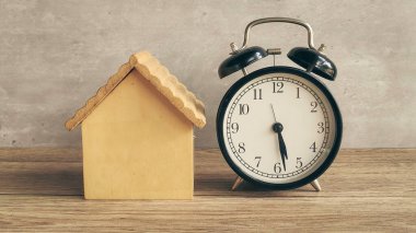 Alarm Clock Next to Wooden House Model Symbolizing Real Estate Deadlines, Time Pressure, and Mortgage Payment Due Dates