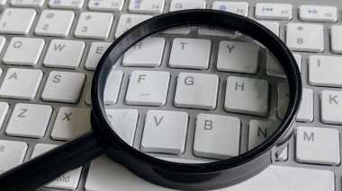 Magnifying Glass on White QWERTY Keyboard for Digital Search and Online Investigation Concept