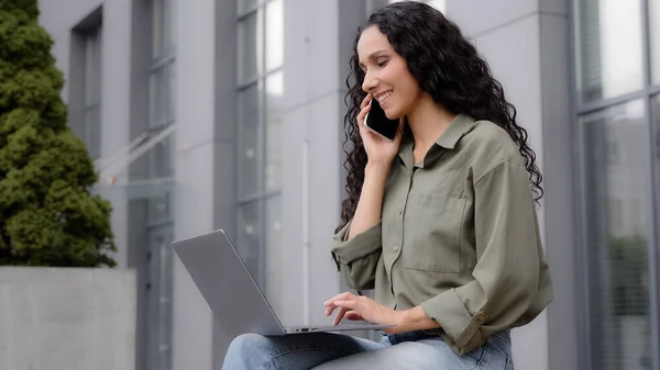 サイドビューマルチタスクビジネス女性フリーランスワーカー女性屋外に座って話す携帯電話入力ノートパソコン回答電話予約注文Eコマースショッピングオンラインで無線コンピュータアプリ — ストック写真