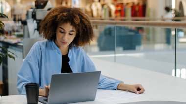 Afrika kökenli Amerikalı öğrenci kız milenyum iş kadını kadın serbest çalışan kullanıcı yöneticisi kafeteryada oturmuş kahve içiyor dizüstü bilgisayarla çalışıyor internetten internete girip interneti kuruyor.