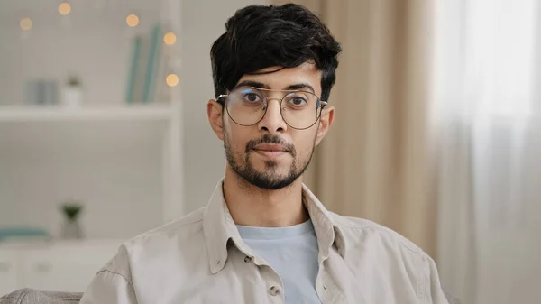 Calm portrait close-up bearded face millennial arabic indian man guy with glasses looking at camera smiling waving nods head answering yes positive decision agreement support approval sitting at home
