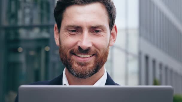 ノートパソコンの画面を見て笑顔ハンサムな若い男幸せなビジネスマンサーフィンインターネット屋外の男性ジャーナリスト記事を書くエージェントコンサルタント電子メールに応答するクライアントと通信する — ストック動画