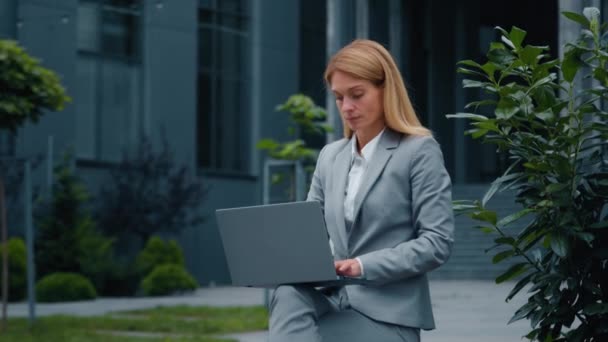 屋外で働くラップトップを入力する集中深刻なビジネス女性の専門家のリーダーは 画面を見てコンピュータアプリケーションを使用してインターネット上の路上で座っている新しいスタートアッププロジェクトを作成します — ストック動画