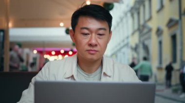 Odaklanmış Asyalı turist dışarıda oturmuş bilgisayarında sosyal ağı tarıyor ücretsiz kablosuz internet seyahat blogcusu kullanıyor bilgisayardan online bilet siparişi veriyor uzaktan çalışan serbest çalışan
