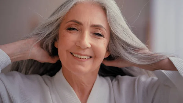 ゴージャス美しいです60歳中年白人女性おばあちゃんシニア50代女性笑顔見てカメラでホーム甘やかすタッチ灰色の髪を楽しむ健康的なヘアケア手順 — ストック写真