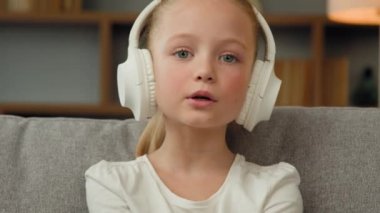 Neşeli küçük beyaz çocuk, neşeli komik çocuk kanepede dinleniyor. Kablosuz kulaklıkla müzik dinliyor. Müzisyenlerin en sevdiği müzik listesi popüler şarkı müzik hobisi.