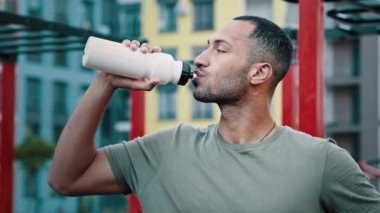 Atletik adam Latin Amerikalı sporcu sıcak içecek soğuk içecek taze su sağlıklı protein içeceği yaz günü susuzluğunu gidermek için şehir spor sahasındaki idmandan sonra dinlendirici konsept konsepti geliştirdi.