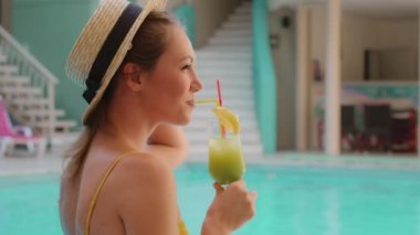 Kaygısız sarışın güzel kadın mayolu seksi bayan manken ve beresi temiz suyla havuz kenarında dinleniyor tropik kokteyl içen kadın turist güneş banyosu yapıyor sıcak yaz gününün tadını çıkarıyor.