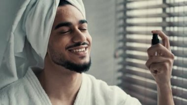 Komik adam, güzel erkek prosedürü. İspanyol sakallı Latin adam banyoda havlu takıyor yüz sıvısı sıkarak mükemmel cilt bakımı kırışıklık önleyici yüz spreyi